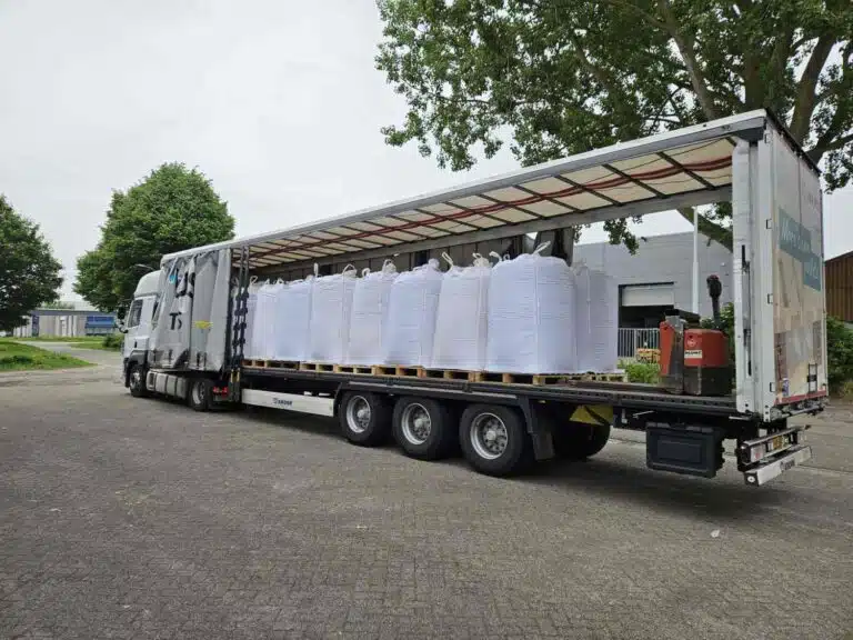 Geopende DTC tautliner oplegger geladen met witte big bags op pallets, veelzijdig wegtransport door De Transport Compagnon.