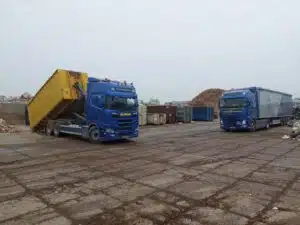 Containerauto met gele afvalcontainer van De Transportcompagnon op recyclingterrein in Surhuisterveen.