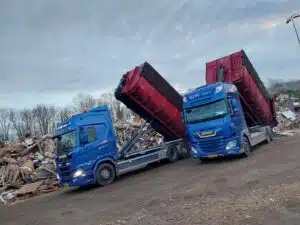 Twee containerauto's van De Transportcompagnon lossen bouw- en sloopafval op verwerkingslocatie.