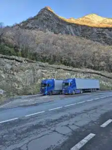 Twee blauwe DTC tautliner-vrachtwagens geparkeerd langs bergweg tijdens internationaal wegtransport door de bergen.