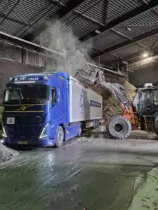KDTC Group Volvo walking floor truck wordt gelost door Hitachi shovel in loods tijdens bulktransport voor DTC.