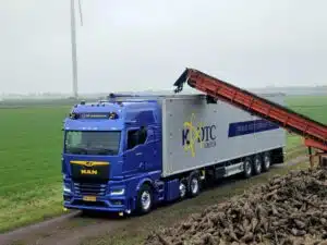 Blauwe MAN vrachtwagen van KDTC Group wordt geladen met suikerbieten via transportband op landweg in Nederland.
